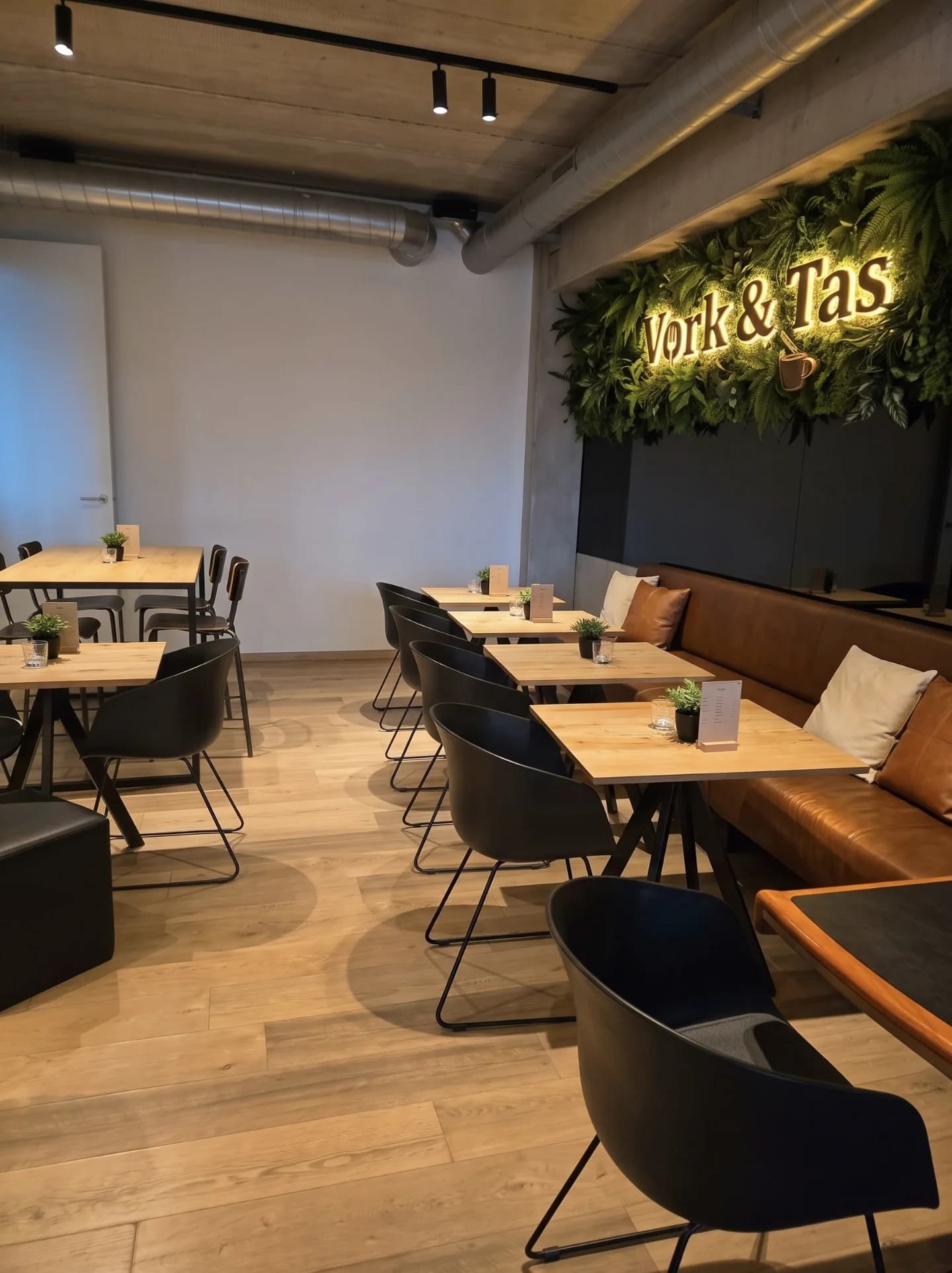 De zaal met houten tafels, een bank in cognac leer en de groene muur met het logo